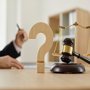 Wooden question mark, gavel, and scales of justice for estate planning questions.